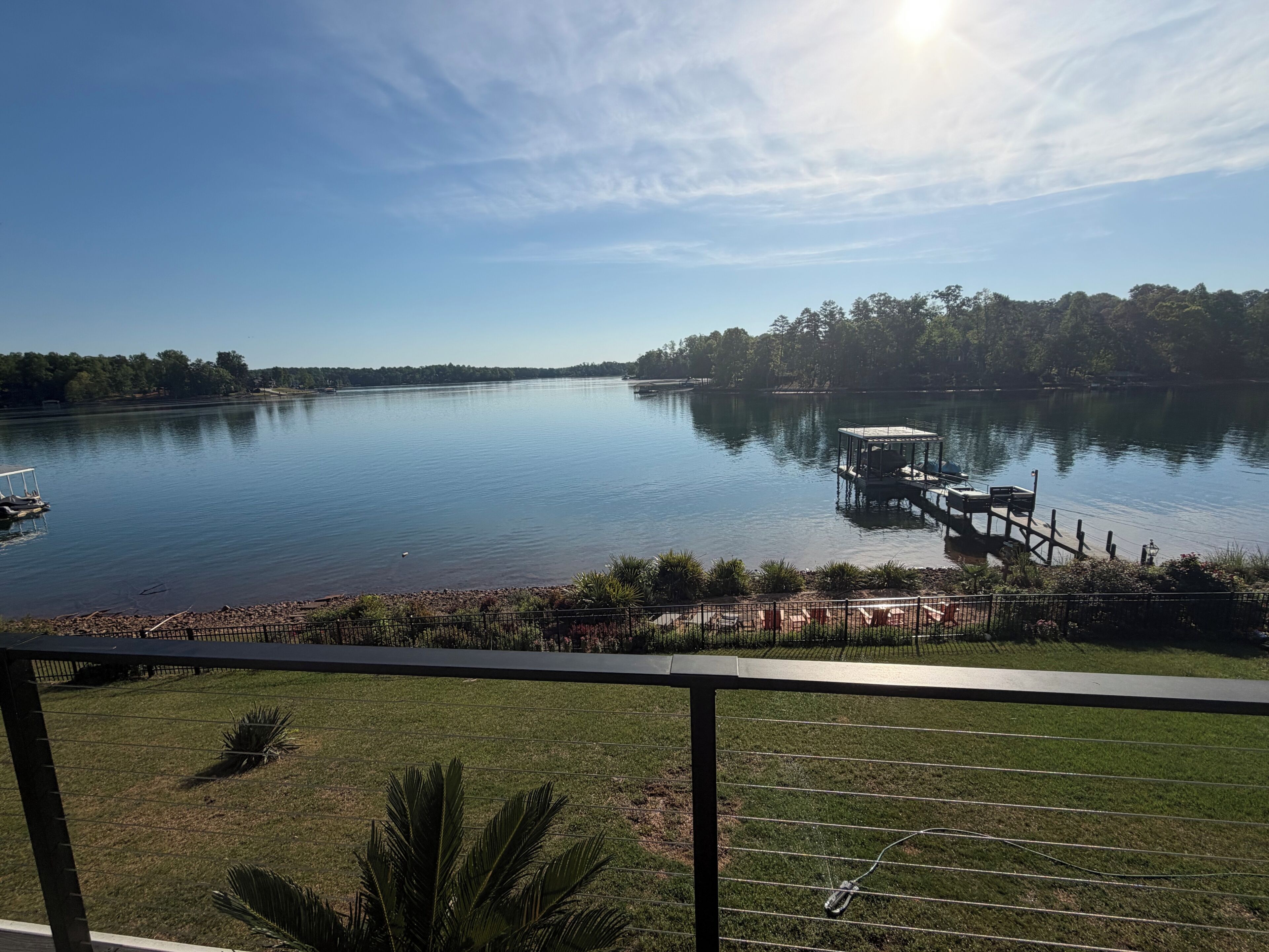 A lake with a dock, a boat, and a grassy area with a fence.