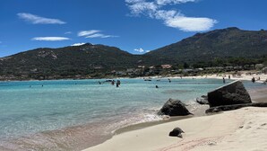 Una playa con agua turquesa cristalina, afloramientos rocosos y una montaña al fondo.