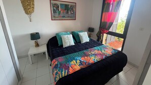 Un dormitorio con una cama, dos mesitas de noche, una lámpara de noche, un ventanal con cortinas y una obra de arte colgada en la pared.