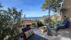 Un patio con una silla de descanso y un reposapiés, una planta grande en maceta, y vista al mar.