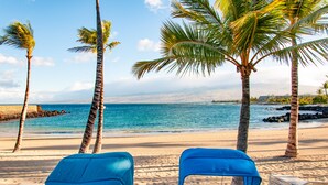 Una playa con dos sillas azules para tomar el sol, vistas despejadas del océano y palmeras.