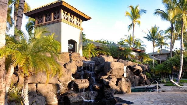 Un resort con cascada de roca, palmeras, piscina y zona de descanso.