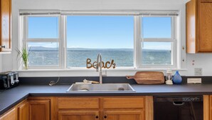 A kitchen with a large window overlooking the sea, a wooden cabinet, a toaster, and a sink.