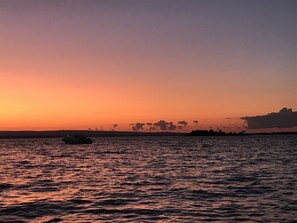 A sunset over a calm body of water with a boat and distant land. - Family Friendly Lake Front Property on the Water's Edge.  Spectacular Setting. (South Hero)
