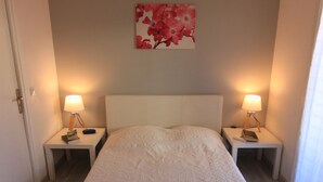 Una cama bien hecha con un cabecero blanco y dos mesitas de noche, cada una con una lámpara y un libro.