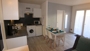 Cocina compacta con cafetera, microondas y lavadora. Cuenta con un comedor, una mesa, sillas y un ventanal.