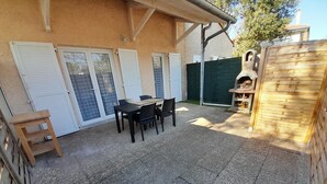 Un patio con una mesa, sillas, un taburete de madera y una parrilla.