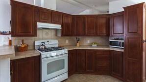 Uma cozinha com armários de madeira, fogão, micro-ondas e painel de azulejos.
