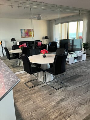 Un salon moderne avec un coin repas, une grande télévision et une vue sur l’océan.