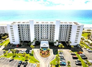 A multi-story hotel with a central courtyard, parking area, and a view of the ocean.