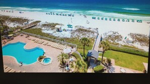 An aerial view of a beach resort with a swimming pool, beach umbrellas, and a lifeguard tower. - Bright, Modern & Beach Front. Amazing gulf views! Beach Retreat @ Sterling Sands (Destin)