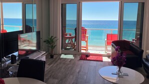 A modern hotel room with a large balcony, a TV, a desk, and a dining area with red chairs. - Bright, Modern & Beach Front. Amazing gulf views! Beach Retreat @ Sterling Sands (Destin)