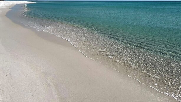 A beach with clear turquoise water and a long pier extending into the ocean. - Bright, Modern & Beach Front. Amazing gulf views! Beach Retreat @ Sterling Sands (Destin)