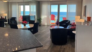 A modern hotel room with a large balcony, a dining area, and a seating area with a view of the ocean. - Bright, Modern & Beach Front. Amazing gulf views! Beach Retreat @ Sterling Sands (Destin)