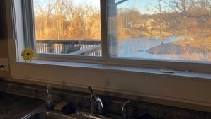 A kitchen with a window overlooking a backyard with a wooden deck and a house. - 3 Bedroom, full kitchen and remodeled bathroom. Water-views from the Kitchen and covered deck. (Caseyville)