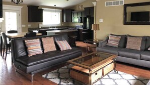 A modern living room with a sofa set, a coffee table, and a kitchen in the background. - 3 Bedroom, full kitchen and remodeled bathroom. Water-views from the Kitchen and covered deck. (Caseyville)
