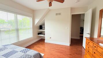 A bedroom with a bed, wooden dresser, ceiling fan, and a window with blinds.