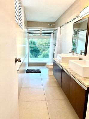 Un baño moderno con un ventanal grande, una ducha y dos lavamanos.