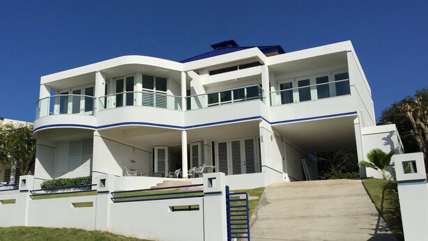 A modern two-story building with a curved facade, balconies, and a covered outdoor area. - OCEAN VIEW VILLA WITH PRIVATE POOL ,STEPS FROM SECLUDED BEACH, GATED COMMUNITY! (Yabucoa)