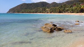 A beach with clear shallow waters, rocky outcrops, and a distant mountain range. - OCEAN VIEW VILLA WITH PRIVATE POOL ,STEPS FROM SECLUDED BEACH, GATED COMMUNITY! (Yabucoa)