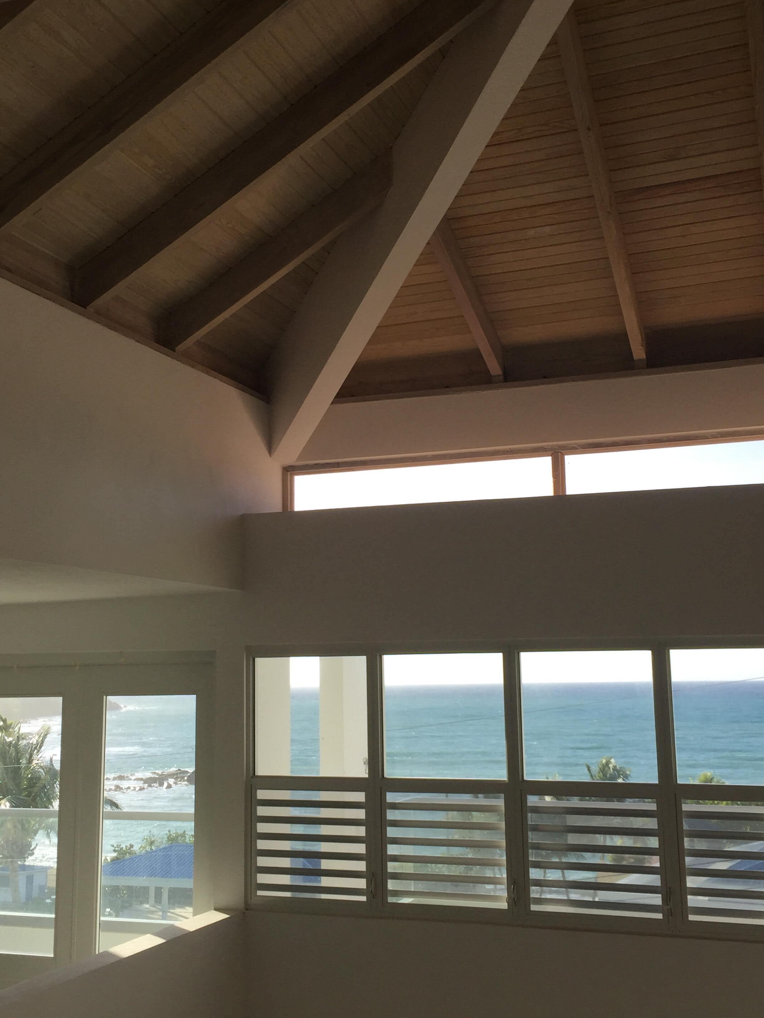 A room with a sloped ceiling, large windows with horizontal blinds, and a view of the ocean.