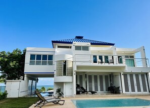 Una casa moderna de dos pisos con piscina, ventanas amplias y un balcón.
