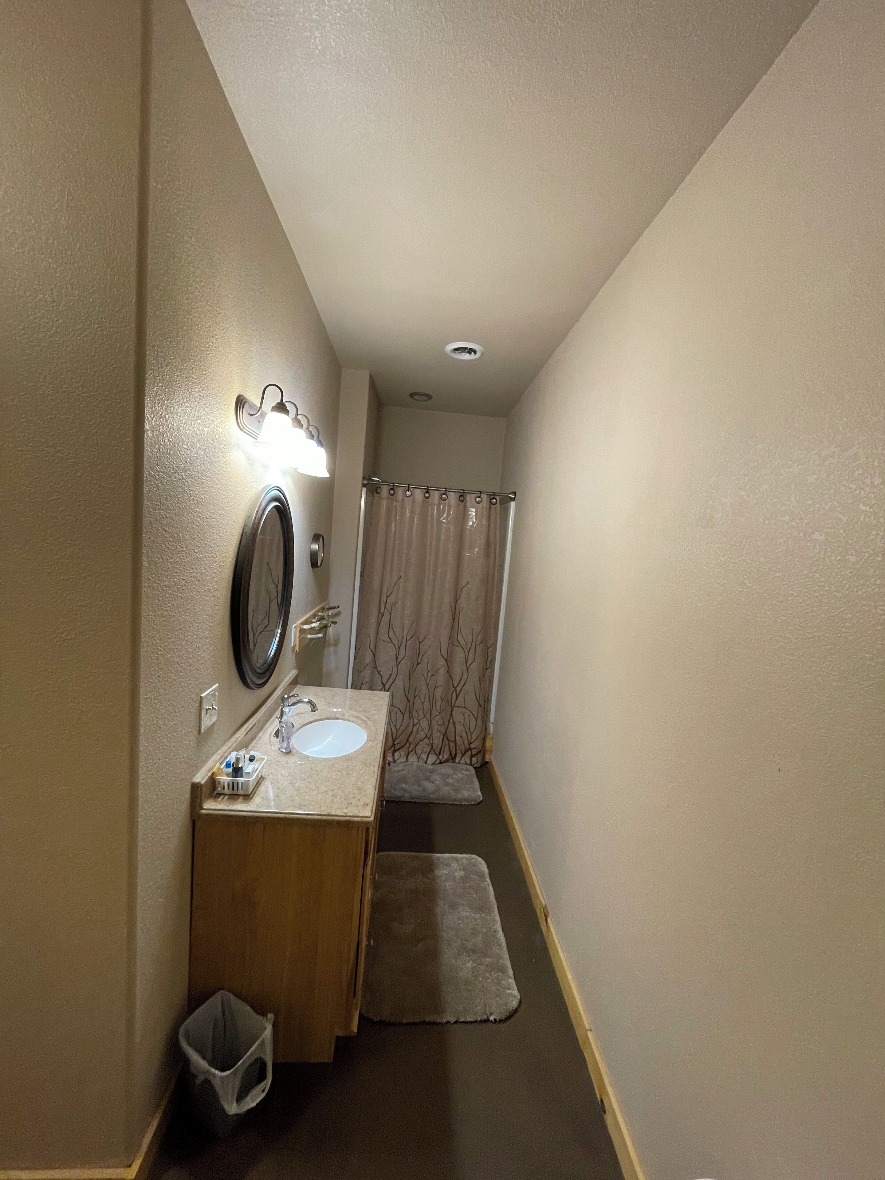 Un pasillo estrecho que conduce a un baño con lavamanos, espejo y cortina de ducha.