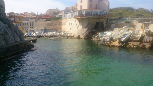 Un pueblo costero con un puerto deportivo, edificios y un litoral rocoso.