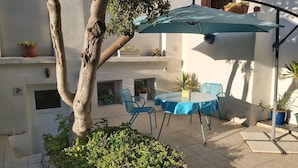 Un patio con mesa y sillas, un árbol y plantas en macetas.