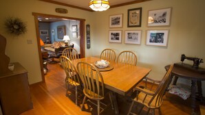 A dining room with a wooden table and chairs, a chandelier, framed photographs on the wall, and a sewing machine on a side table. - Charming Cannon Beach Cottage- Perfect Family Getaway near the beach! (Cannon Beach)