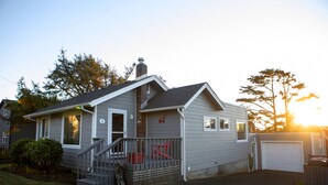 A single-story house with a front porch, a garage, and a small front yard. - Charming Cannon Beach Cottage- Perfect Family Getaway near the beach! (Cannon Beach)