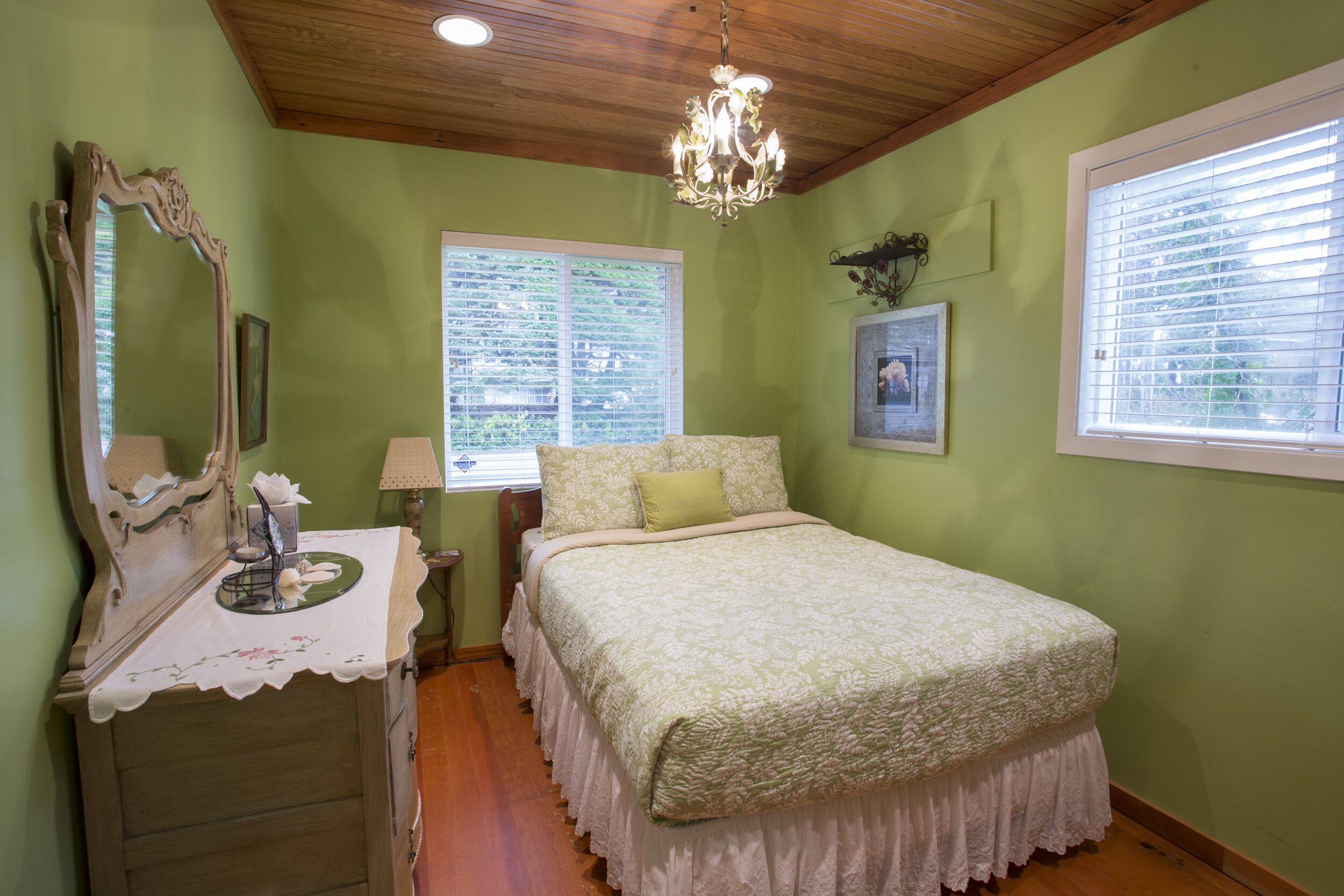 Une chambre à coucher avec un lit, une commode, un miroir, un lustre et des fenêtres.