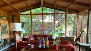 Un salon chaleureux avec un canapé rouge, une table basse en bois et une grande fenêtre donnant sur la forêt.