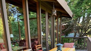Une terrasse extérieure couverte, dotée d’une table et de chaises, et entourée de portes et de fenêtres en verre.
