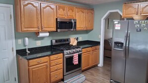 A kitchen with wooden cabinets, a stainless steel refrigerator, a microwave, a stove, and a sink. - Old Wagon Lodge | Spacious Retreat | WiFi & Hot Tub + Theater Room (Luray)