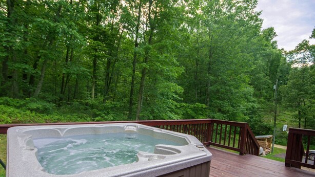 A hot tub on a wooden deck surrounded by a forest. - Old Wagon Lodge | Spacious Retreat | WiFi & Hot Tub + Theater Room (Luray)