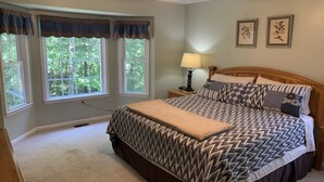 A bedroom with a bed, a nightstand, a lamp, and two windows with curtains. - Old Wagon Lodge | Spacious Retreat | WiFi & Hot Tub + Theater Room (Luray)