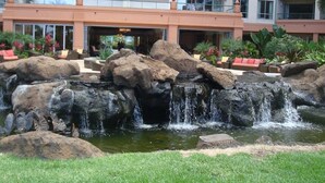 A hotel with a rock waterfall feature, outdoor seating, and a well-maintained garden. - Klvr presents Honua Kai Resort K238*Quiet location (Lahaina)