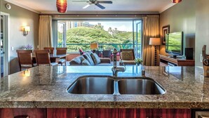 A modern kitchen with a granite countertop, stainless steel sink, and wooden cabinets. - Klvr presents Honua Kai Resort K238*Quiet location (Lahaina)