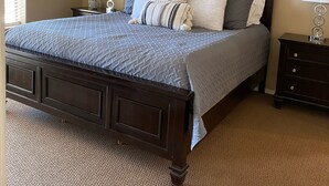 A bedroom with a large bed, dark wood headboard, two bedside tables with lamps, a decorative wall piece, and a textured carpet.