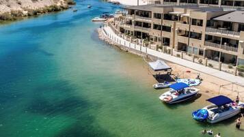 A coastal hotel with a marina, clear waters, and mountains in the background.
