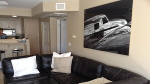 A living room with a black leather sofa, a white pillow, and a framed black and white photograph on the wall.