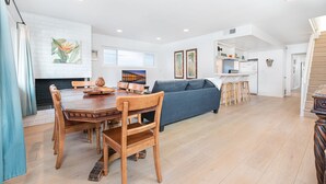 Amplia sala de estar con una mesa de comedor, sofá azul y cocina al fondo.