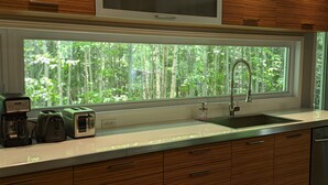 A kitchen with a large window, a sink, a toaster, a coffee maker, and wooden cabinets. - Treehouse, 3 bedrooms (4th bedroom, sleeps 7+), EV terminals. (Petite-Rivière-St-Francois)