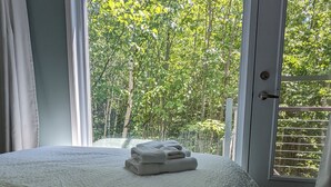A bedroom with a bed, a window with curtains, and a view of trees. - Treehouse, 3 bedrooms (4th bedroom, sleeps 7+), EV terminals. (Petite-Rivière-St-Francois)