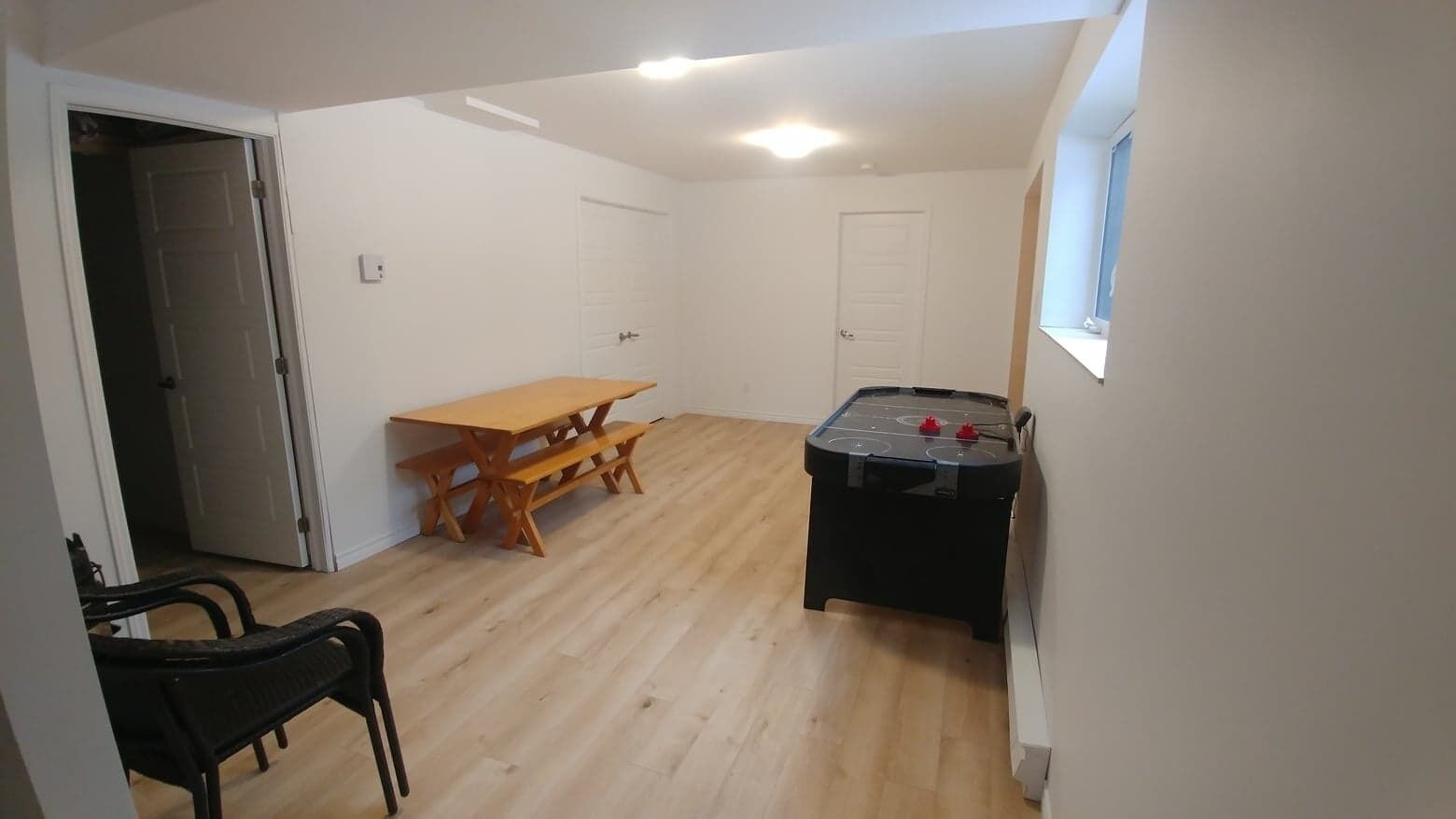 Una habitación con piso de madera, una mesa con bancos, una mesa de billar y una puerta.