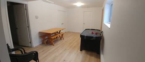 Una habitación con piso de madera, una mesa con bancos, una mesa de billar y una puerta.