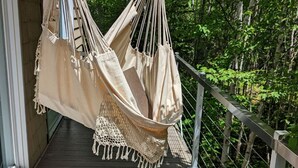 A hammock hanging on a wooden deck with a railing, surrounded by greenery. - Treehouse, 3 bedrooms (4th bedroom, sleeps 7+), EV terminals. (Petite-Rivière-St-Francois)