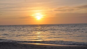 A beach at sunset with the sun reflecting on the water.