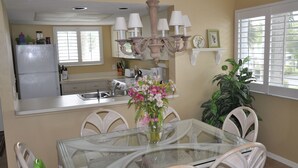A dining area with a glass table and white chairs, a chandelier, and a potted plant.